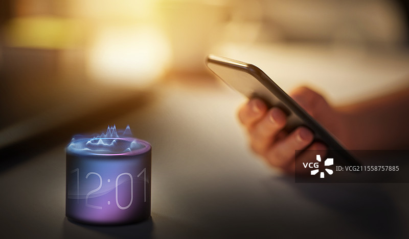虚拟现实、科技和物联网概念 - 夜间办公室中，手持智能手机和智能音箱，音箱上显示时间。图片素材