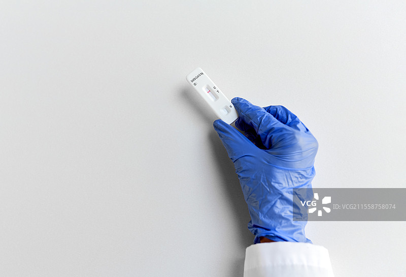 医学、隔离和疫情概念 - 医用手套中的手握着白色背景下的阴性自测新冠病毒检测结果。手部特写显示阴性新冠病毒检测。图片素材