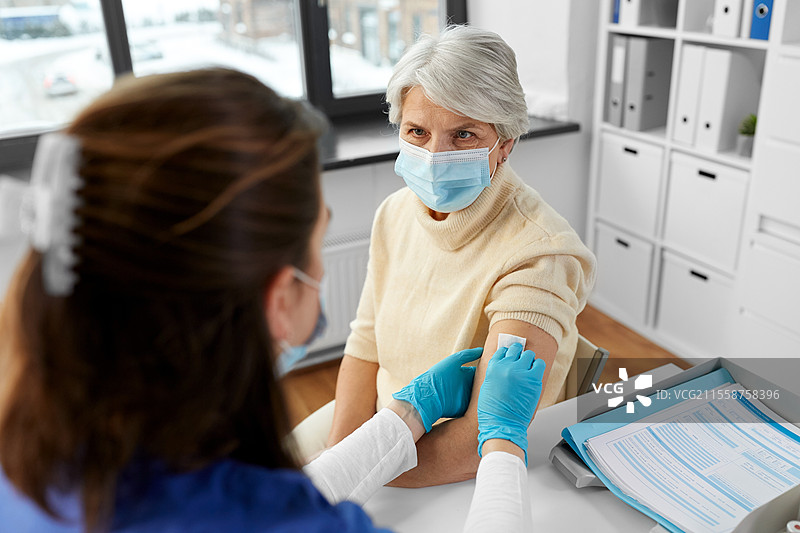 医学、健康和疫苗接种概念 - 医生或护士在医院为戴口罩的老年女性消毒手臂皮肤，准备为她接种疫苗。图片素材