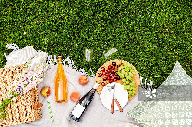 休闲饮品概念 - 食物、饮料和篮子在草地上的野餐毯上的特写。食物、饮料和篮子在草地上的野餐毯上。图片素材