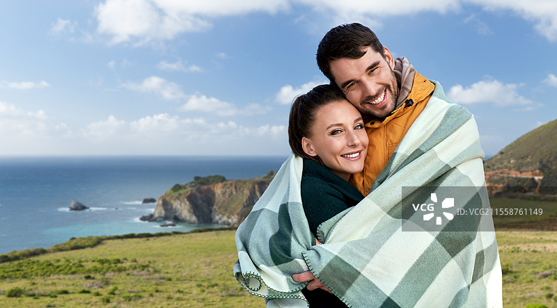 爱情、旅行和旅游概念 - 一对快乐微笑的情侣在加利福尼亚大苏尔海岸背景下裹着温暖的毛毯。图片素材