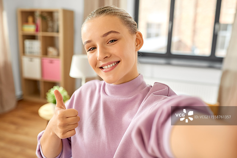 人们、儿童与科技的概念 - 开心微笑的女孩在家自拍并竖起大拇指。女孩在家自拍并竖起大拇指。图片素材