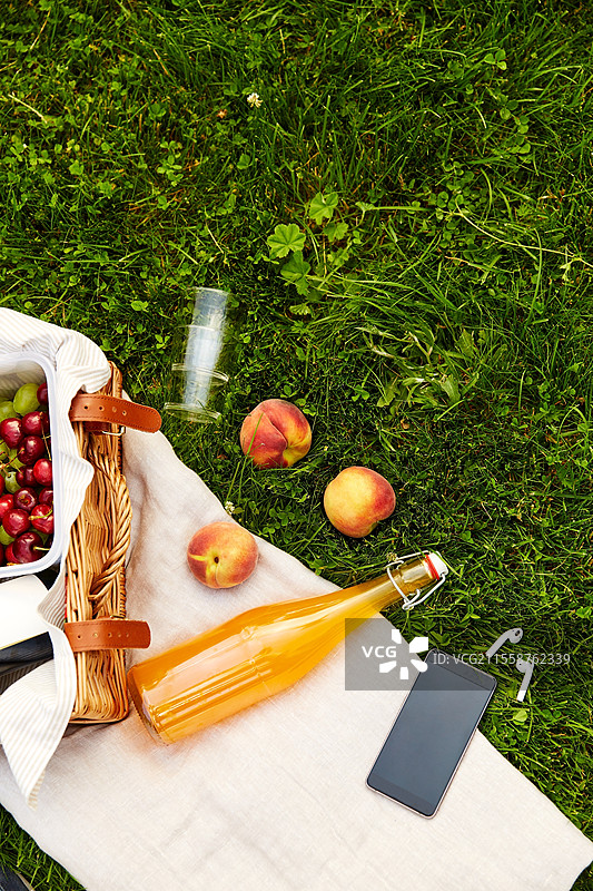 休闲、科技与夏季概念 - 草地上的野餐篮、果汁瓶和带耳机的智能手机特写。野餐篮、果汁瓶、手机和耳机。图片素材