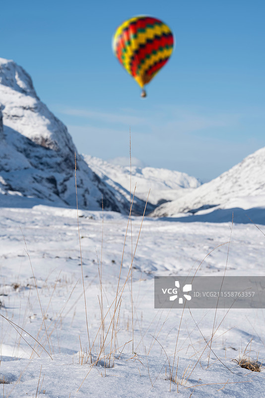 热气球在苏格兰高地的斯托布·迪尔格·布阿凯尔·埃蒂夫·莫尔山上空飞行的数字合成图，展现了令人惊叹的标志性冬季风景。图片素材