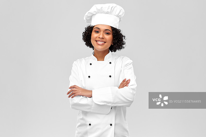 烹饪、烹饪艺术和人们的概念 - 开心微笑的女性厨师穿着白色厨师帽和外套，背景为灰色。微笑的女性厨师穿着白色厨师帽和外套。图片素材