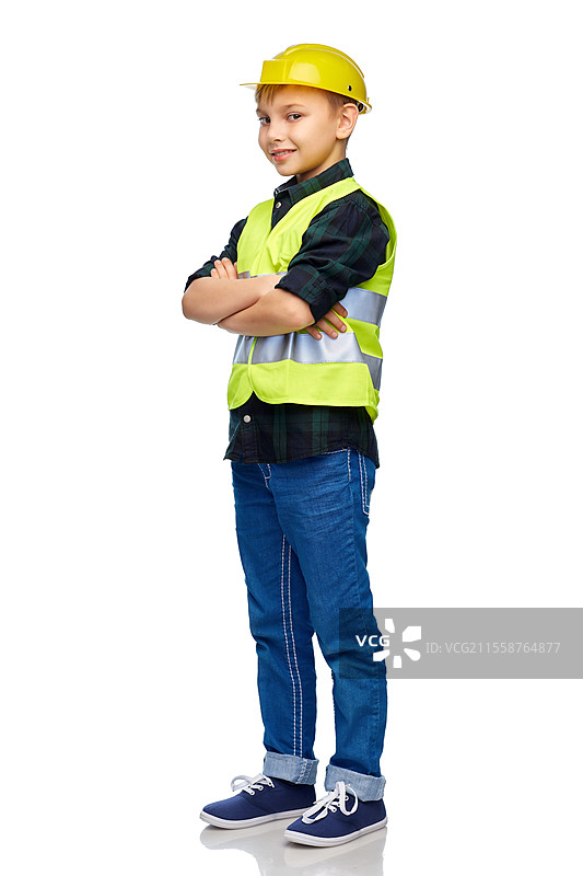 建筑、施工和职业概念 - 开心微笑的小男孩穿着安全帽和安全背心，双臂交叉，背景为白色。小男孩穿着安全帽和安全背心。图片素材