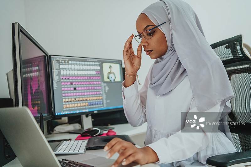 年轻的非裔美国现代穆斯林女商人，佩戴头巾，身处一个创意明亮的办公室，背景有一台大屏幕。高质量照片。图片素材