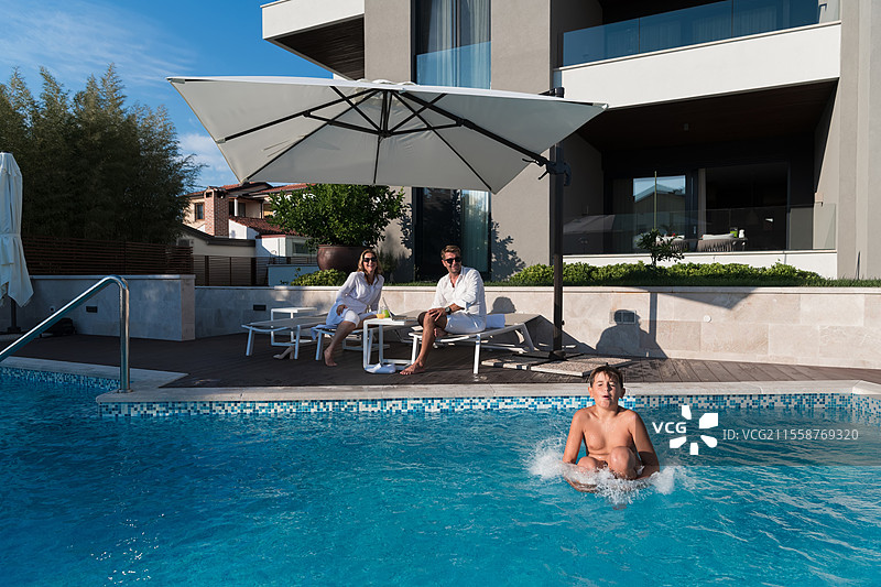 快乐的家庭在豪华别墅和游泳池中享受假期。老年夫妇在假期中与他们的儿子共度时光。选择性对焦。高质量照片。图片素材