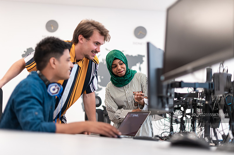 多元文化的初创企业团队，身穿头巾的女性在现代开放式办公室内开会，进行头脑风暴，使用笔记本电脑和台式电脑。选择性聚焦。高质量照片。图片素材