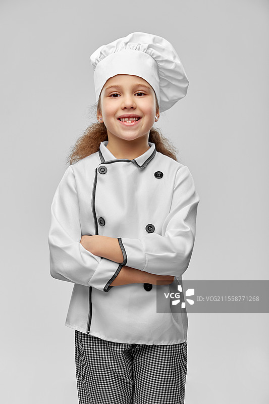 烹饪、烹饪艺术和职业概念 - 开心微笑的小女孩穿着厨师帽和外套，背景为灰色。微笑的小女孩穿着厨师帽和外套。图片素材