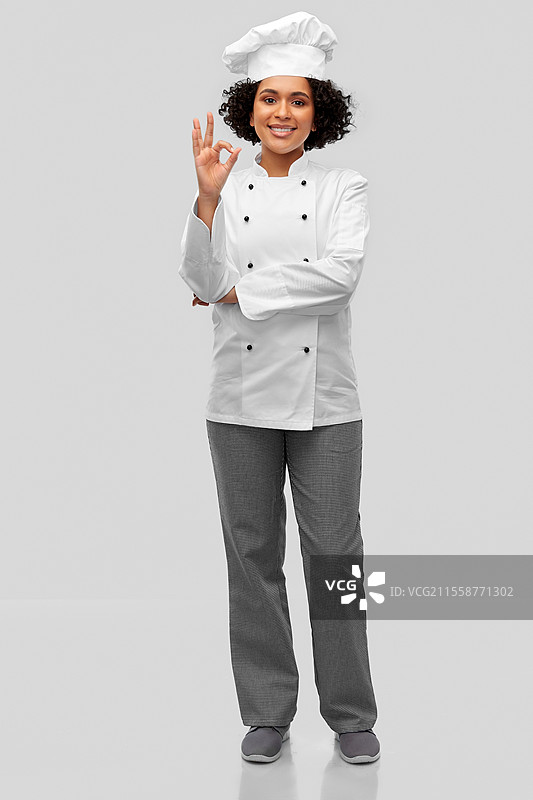 烹饪、烹饪艺术和人们的概念 - 开心微笑的女性厨师穿着白色高帽和外套，在灰色背景下做出“好的”手势。开心微笑的女性厨师做出“好的”手势。图片素材