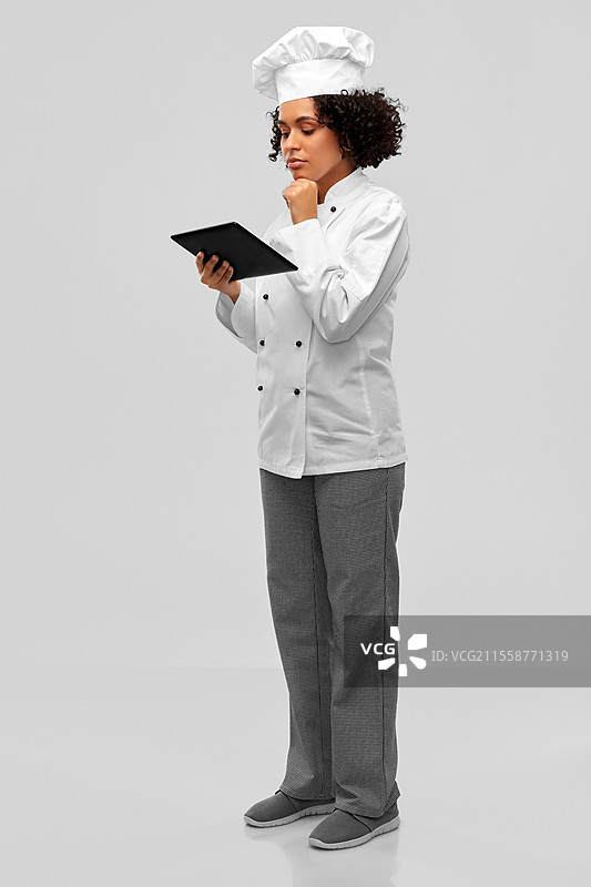 烹饪、烹饪艺术和人们的概念 - 思考中的女性厨师，戴着厨师帽和外套，手持平板电脑，背景为灰色。思考中的女性厨师与平板电脑。图片素材