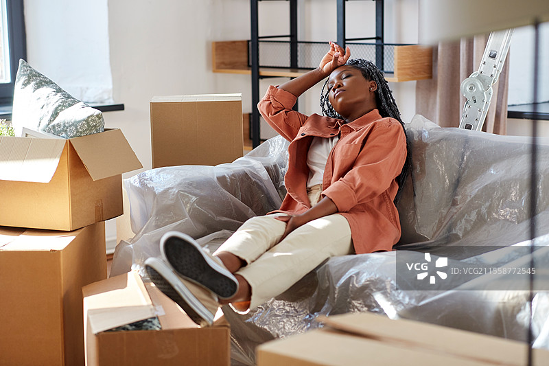 搬家、人物与房地产概念 - 疲惫的女性坐在新家沙发上休息，周围是纸箱。疲惫的女性在搬家时休息。图片素材