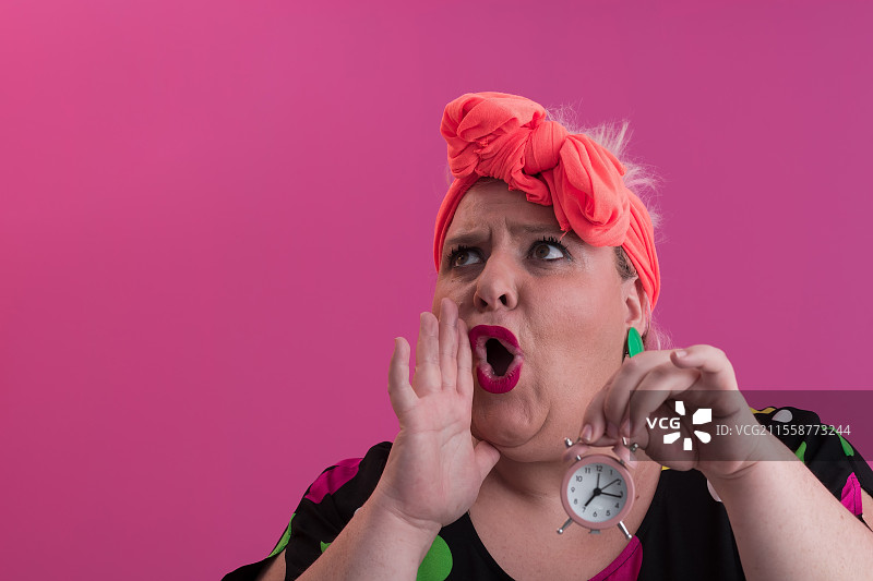 微胖年轻女士微笑着双手拿着沙漏，背景为粉色。高质量照片。图片素材