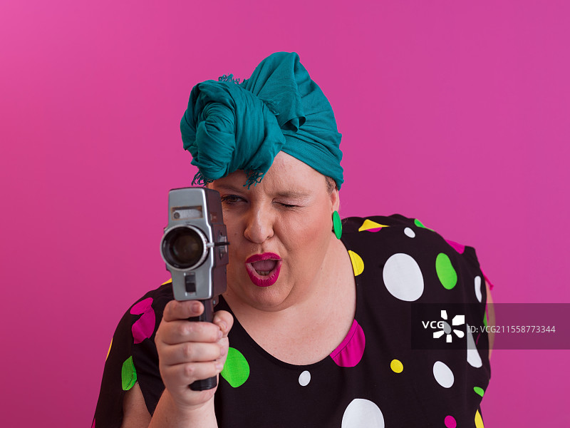 微胖女性穿着裙子，手持复古相机，面带搞笑的情感表情，背景为粉色，旅行者度假，夏季时尚风格，兴奋的游客。高质量照片。图片素材