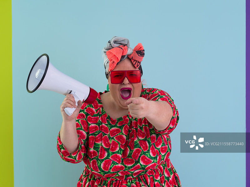 有趣的胖女人在青色背景下摆姿势，手持扩音器大喊。人们的情感生活方式概念。可供模仿的空白空间。高质量照片。图片素材