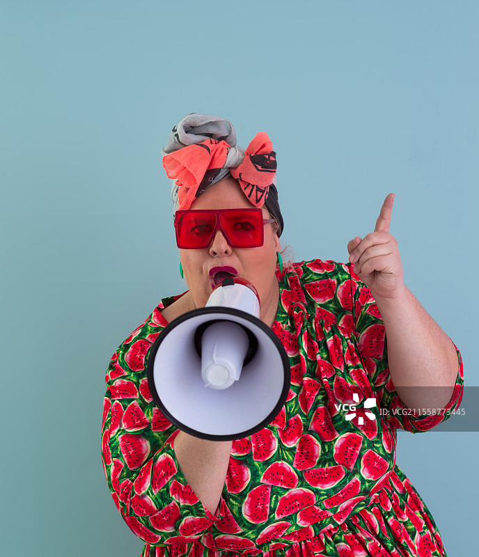 有趣的胖女人在青色背景下摆姿势，手持扩音器大喊。人们的情感生活方式概念。可供模仿的空白空间。高质量照片。图片素材