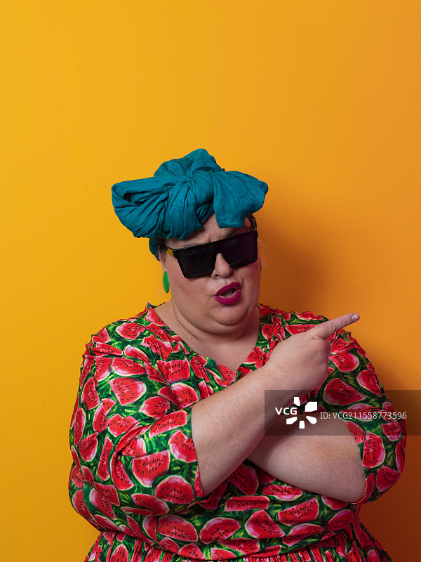 有趣的加大码性感模特，戴着时尚太阳镜，穿着色彩斑斓的裙子，在黄色的福尔图娜金色背景下摆姿势，拍摄于摄影棚。高质量照片。图片素材