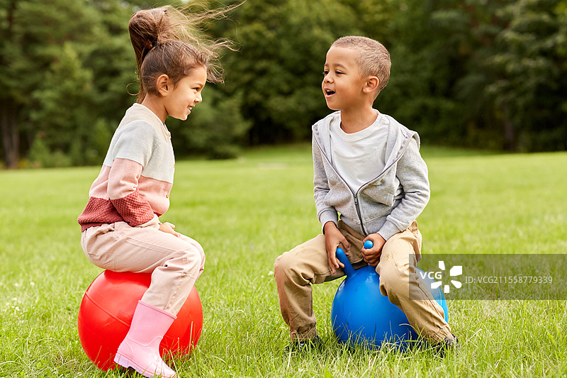 童年、休闲和人们的概念 - 快乐的孩子们在公园里跳跃着蹦蹦球。快乐的孩子们在公园里跳跃着蹦蹦球。图片素材