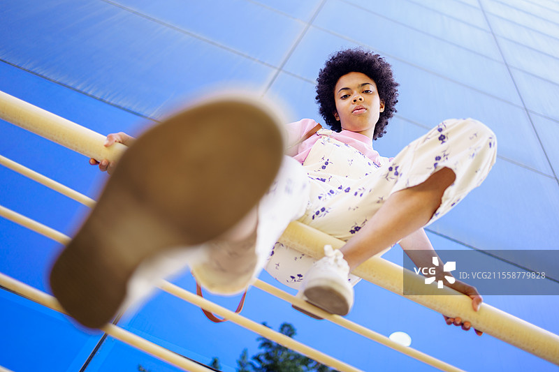 全身非裔美国穿着工装和运动鞋，坐在城市的围栏上看着镜头。黑女人穿着休闲服装坐在栏杆上。图片素材