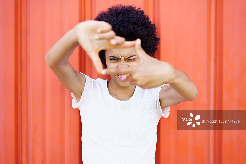 积极的非裔美国，黑色非洲卷发，面对镜头做出框架手势，背景为红色街道。快乐的黑人做出框架手势。图片素材