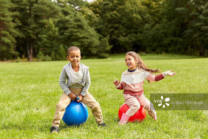 童年、休闲和人们的概念 - 快乐的孩子们在公园里跳跃着蹦蹦球。快乐的孩子们在公园里跳跃着蹦蹦球。图片素材