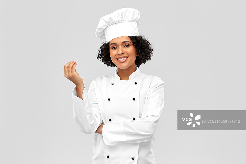 烹饪、烹饪艺术和人们的概念 - 开心的女厨师戴着厨师帽和白色外套，在灰色背景下展示美食标志。开心的女厨师展示美食标志。图片素材