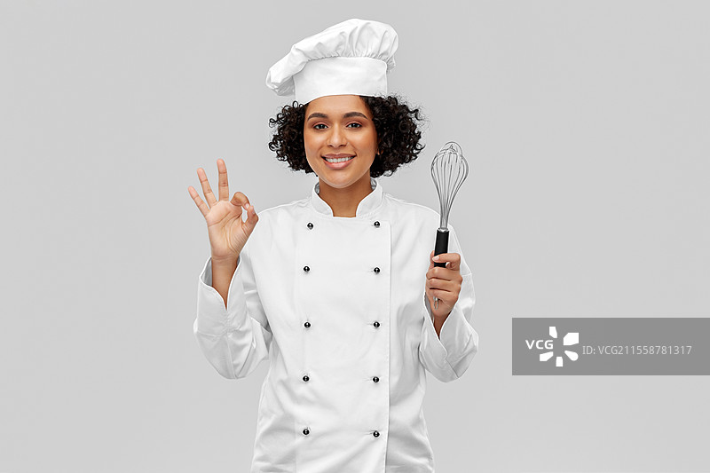 烹饪、烹饪艺术和人们的概念 - 开心微笑的女厨师戴着厨师帽，手持打蛋器在灰色背景下做出“好的”手势。微笑的女厨师手持打蛋器做出“好的”手势。图片素材