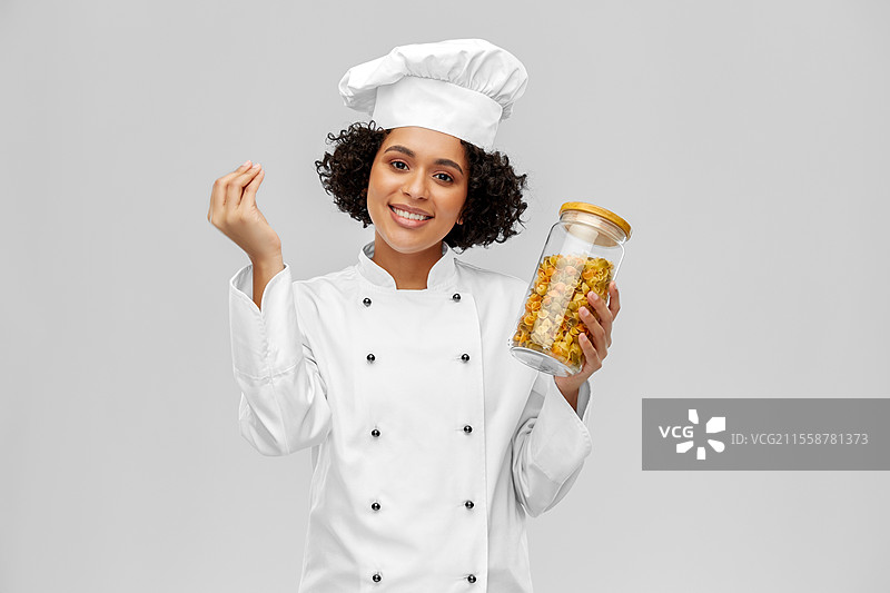 烹饪、烹饪艺术和人们的概念 - 开心微笑的女厨师手持意大利面罐，展示美食手势，背景为灰色。微笑的女厨师手持意大利面罐。图片素材