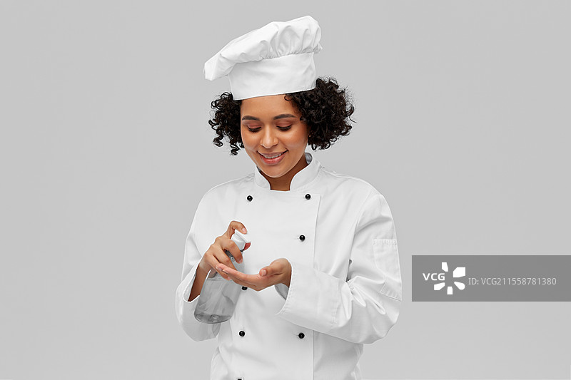 烹饪、烹饪艺术和人们的概念 - 开心微笑的女厨师在灰色背景下使用洗手液或液体肥皂。女厨师正在使用洗手液或液体肥皂。图片素材