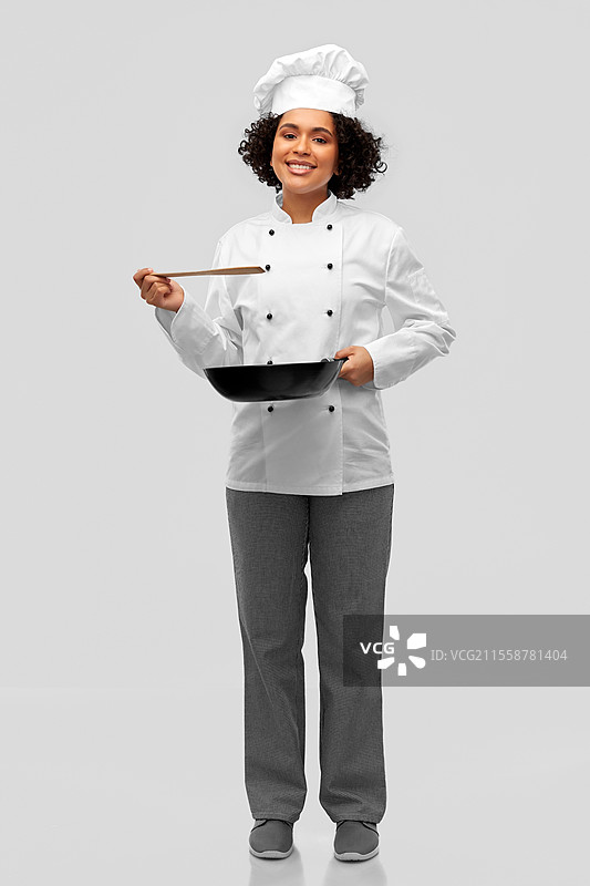 烹饪、美食和人们的概念 - 开心微笑的女厨师手持平底锅，背景为灰色。微笑的女厨师手持平底锅。图片素材