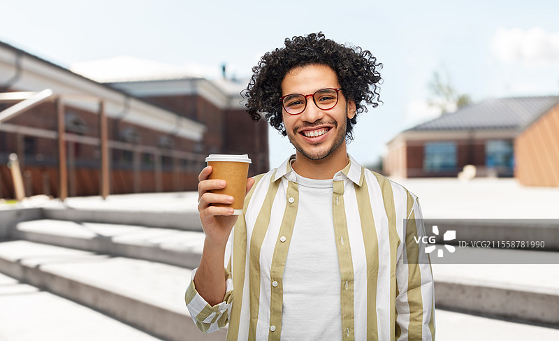 饮品与人群的概念 - 微笑的年轻男子戴着眼镜，手拿外带咖啡杯，背景是城市街道。微笑的年轻男子在城市中手拿外带咖啡杯。图片素材