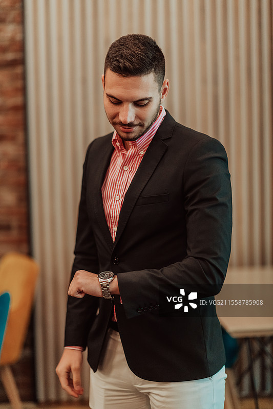 年轻现代经理在现代办公室中摆姿势看着钟表的肖像。选择性对焦。高质量照片。图片素材