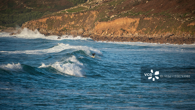 在康沃尔的塞农湾，未被识别的冲浪者在日落时分骑乘海浪图片素材