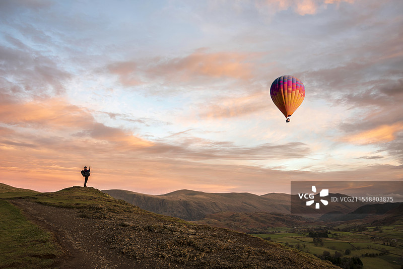 美丽的日落风景，视角来自拉特里格山，俯瞰湖区的格雷特·多德和斯泰巴罗·多德，一名男子正在拍摄风景中的热气球。图片素材