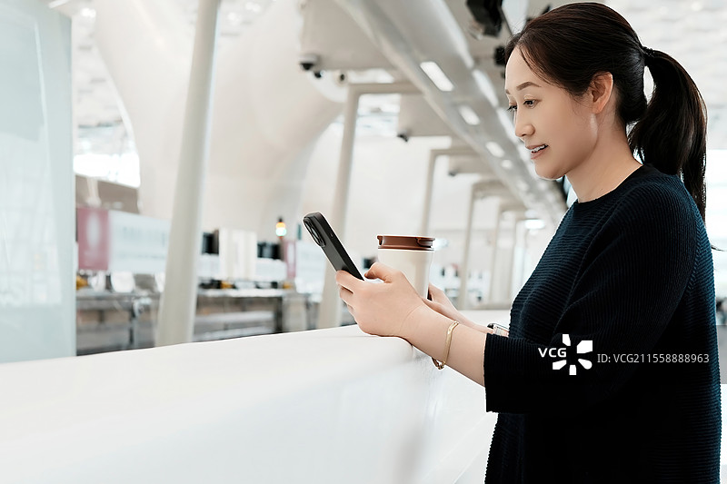 在现代机场环境中使用智能手机和咖啡的女性图片素材