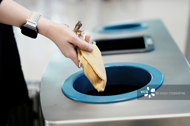 正确处理食物垃圾：一只手把香蕉皮放在垃圾桶里图片素材