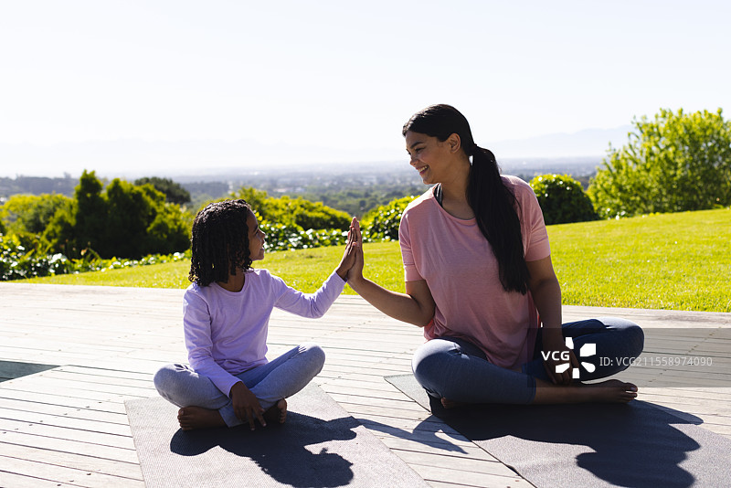 母女俩坐在户外的瑜伽垫上，开心地击掌庆祝图片素材