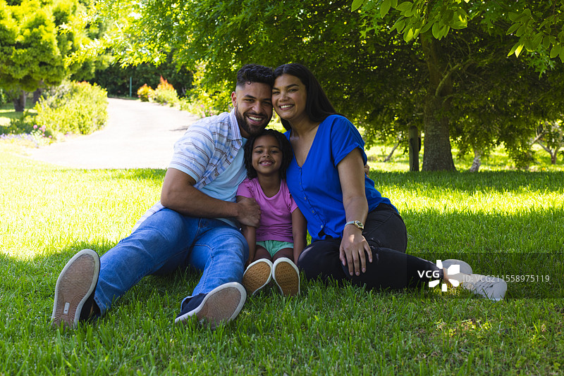 微笑的家庭坐在公园的草地上，共同享受阳光明媚的一天。图片素材