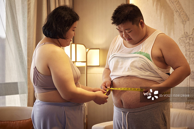 肥胖的青年女人为伴侣测量腰围图片素材