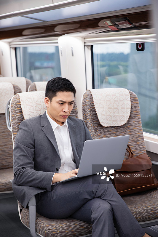 高铁车厢内坐在座位上使用笔记本电脑的青年男人图片素材