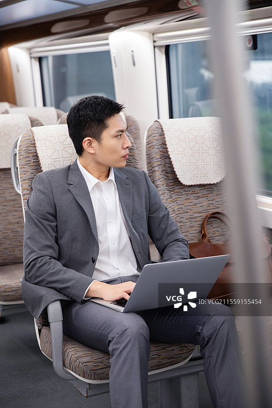 高铁车厢内坐在座位上使用笔记本电脑的青年男人图片素材