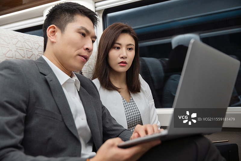 高铁车厢内坐在座位上使用笔记本电脑的两位青年商务人士图片素材