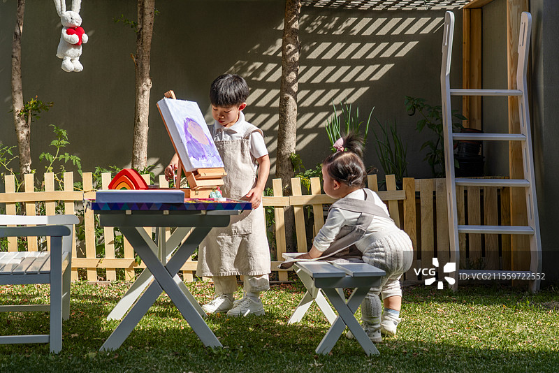 院子里一岁小女孩看小哥哥画画图片素材