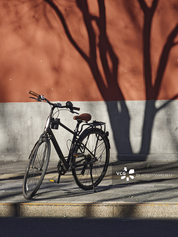 晴朗的天气，北京胡同里的红墙和墙上的树影，以及墙下的自行车。图片素材