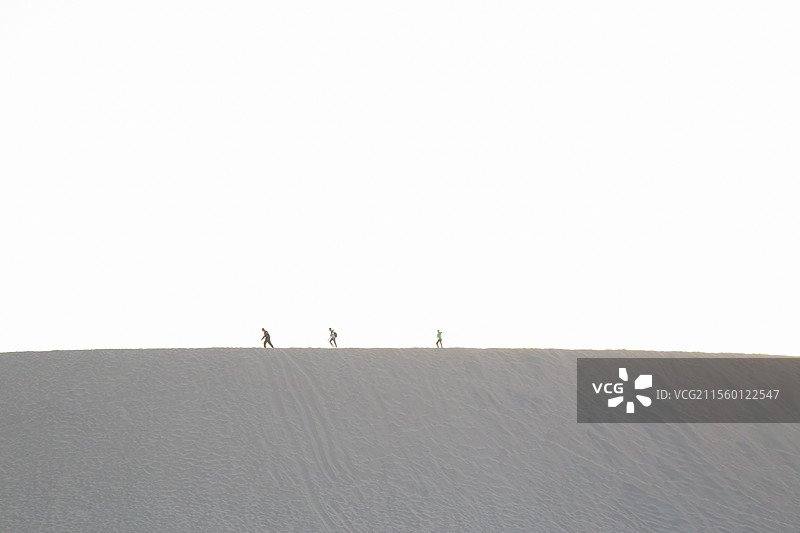 甘肃省敦煌市鸣沙山沙漠中三人行走的身影图片素材