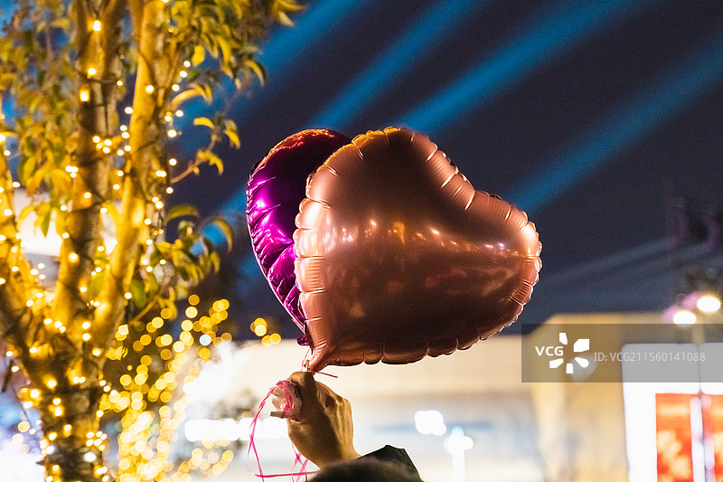 夜晚，霓虹灯的映照下，天空背景下仰视手拿心形气球的庆祝特写图片素材