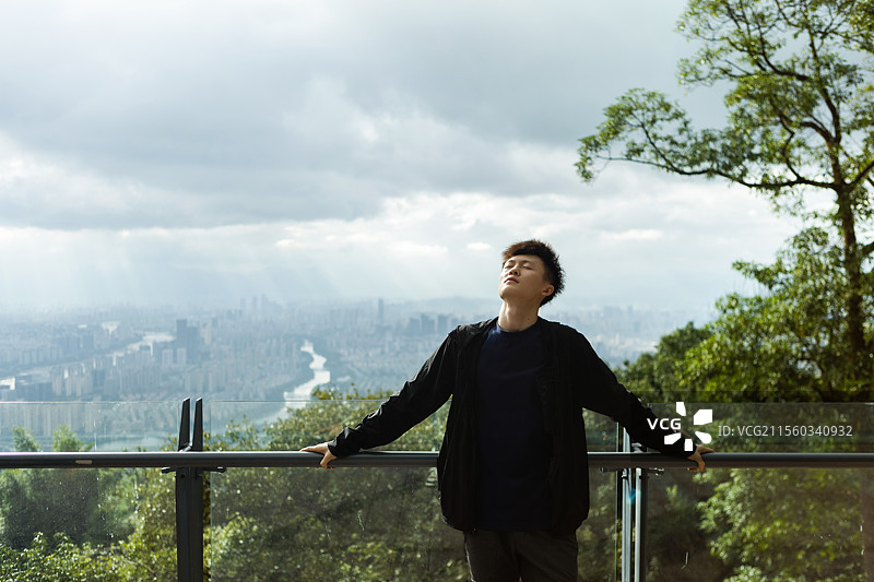 一位青年站在山顶眺望远方的城市天际线，象征自由、探索与旅行精神。图片素材