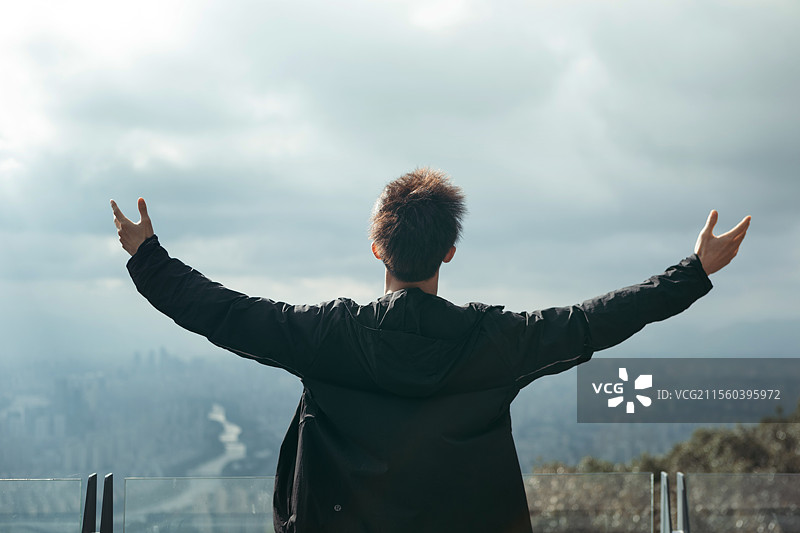 一位青年站在山顶眺望远方的城市天际线，象征自由、探索与旅行精神。图片素材