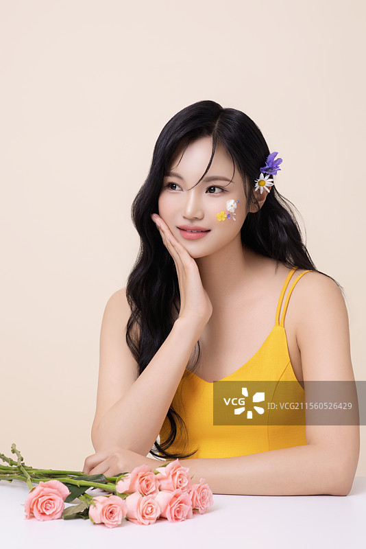 一位美丽的女性，脸上涂有彩绘，头戴花朵，坐在一张桌子前，桌上摆放着一束花。图片素材